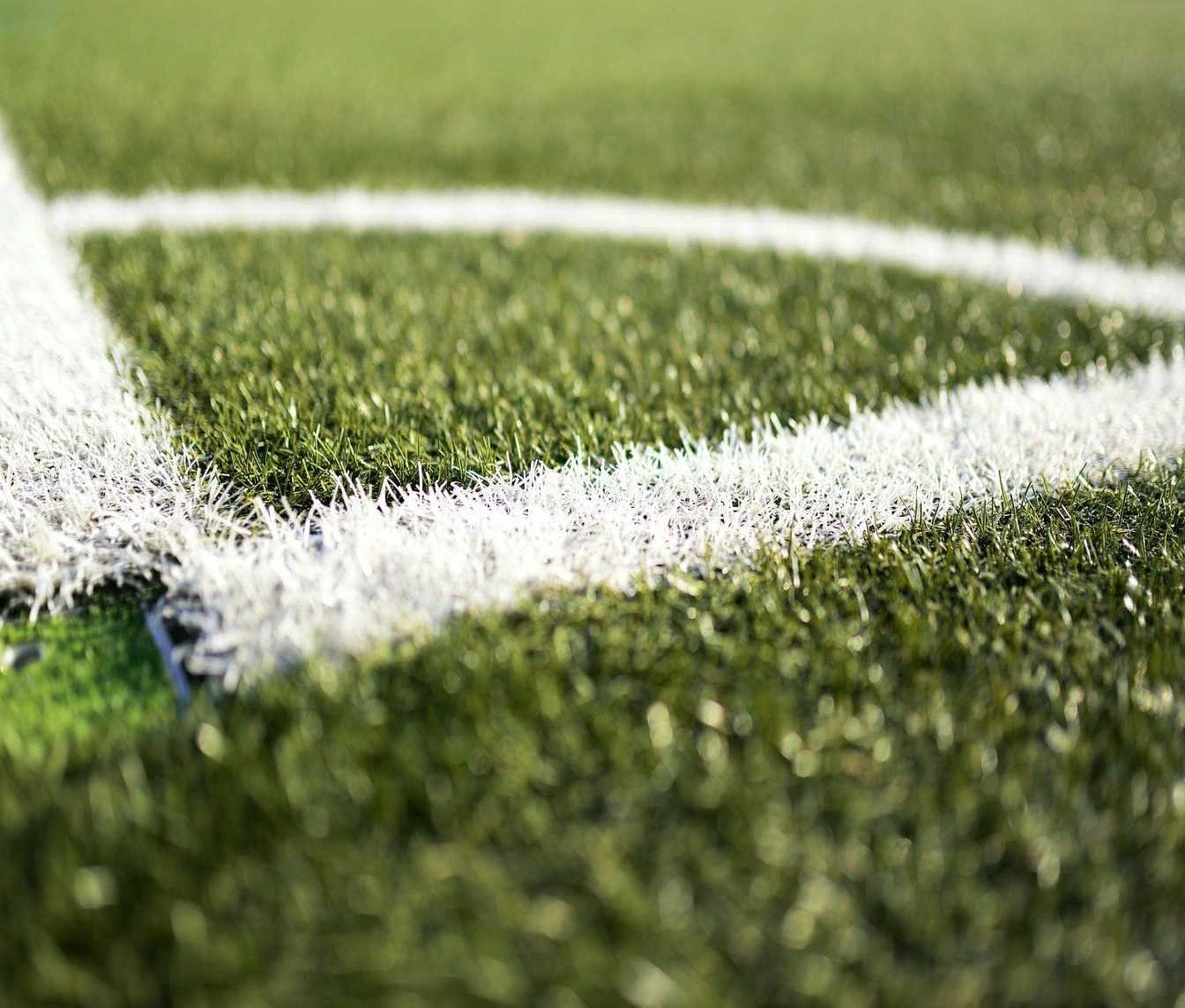 Close-up of a synthetic grass soccer field in Maricopa AZ, focused on the white lines marking a corner of the pitch. The texture of the artificial turf and the precise maintenance by Maricopa Turf Pros are evident. The background is slightly blurred to emphasize the markings.
